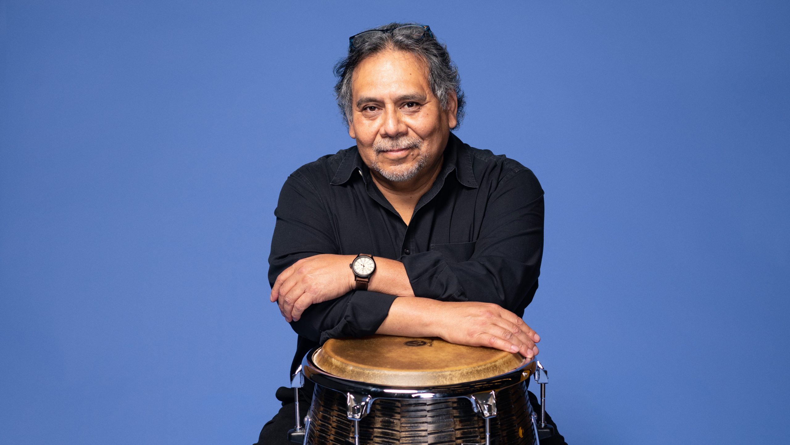 Felix Contreras seated, leaning with his arms resting on a large drum.